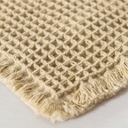 Close-up of a textured beige rug with a diamond pattern on a light gray background