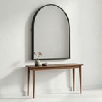 Wooden console table with a large arch-shaped mirror on a white wall.