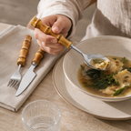 Person using bamboo handle spoon with homemade soup at a dining table.