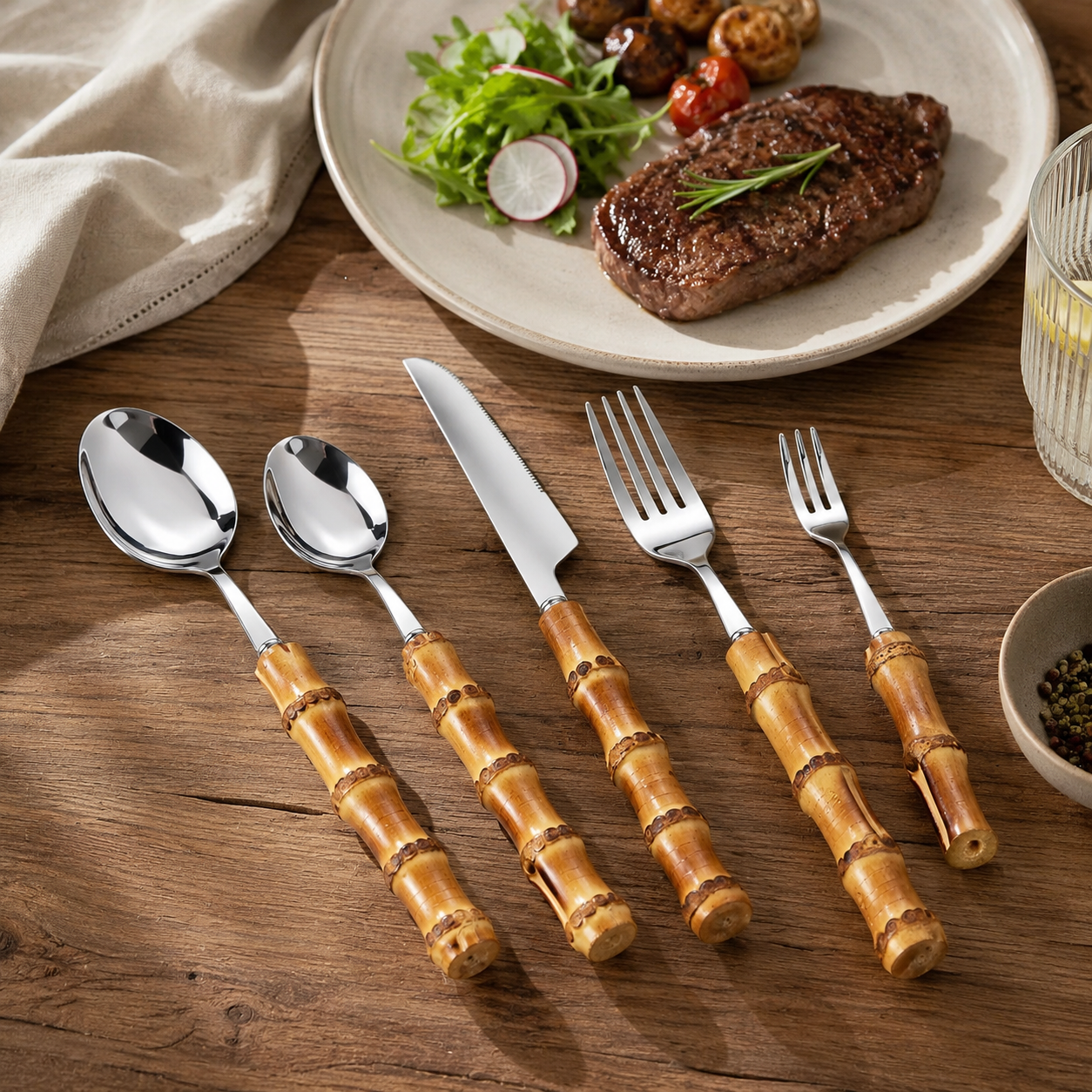 Bamboo handle cutlery set displayed beside a steak dinner on a rustic wooden table.