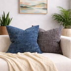 Two textured throw pillows on a couch with a landscape painting in the background.