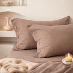 Two brown pillows on a bed with a candle and decorative items in the background.