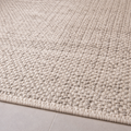 Close-up of a textured beige rug on a light gray floor.