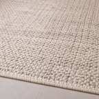 Close-up of a textured beige rug on a light gray floor.