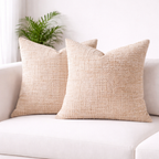 Two beige textured pillows on a white sofa with a plant in the background