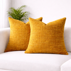 Two mustard yellow textured pillows on a white couch with a plant in the background.
