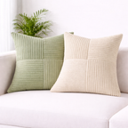 Two textured pillows, one green and one beige, on a white couch with a plant in the background.