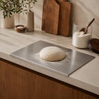 Bread dough on a metal tray with flour on a kitchen counter.