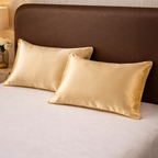 Two gold satin pillows on a bed with a brown headboard.