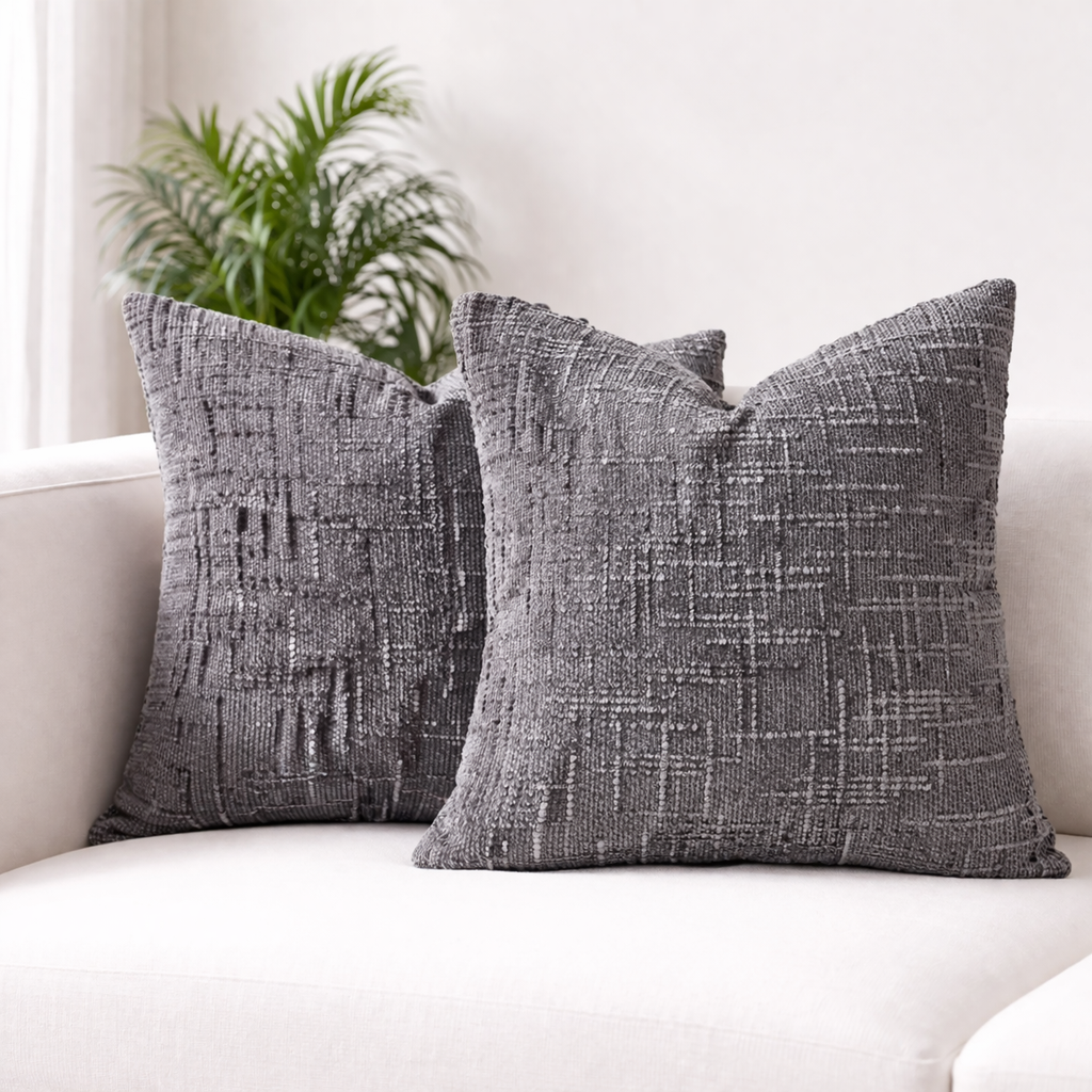Two gray textured pillows on a white couch with a plant in the background.