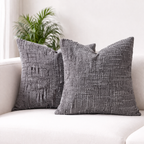 Two gray textured pillows on a white couch with a plant in the background.