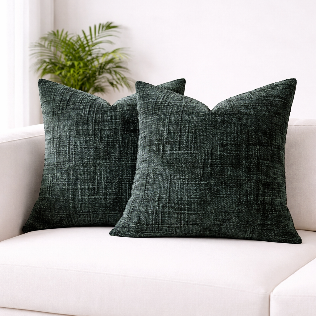 Two dark green textured pillows on a white couch with a plant in the background.