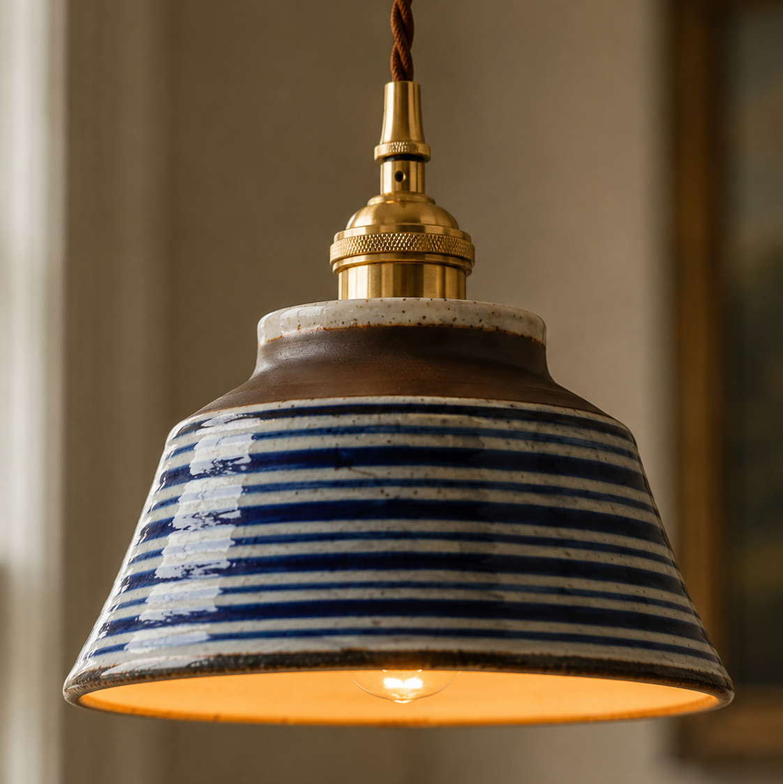 Pendant light with striped ceramic shade and brass fitting against a neutral background