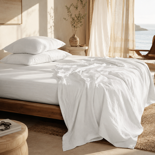 Neatly made bed with white linen sheets bedding in a bright bedroom.