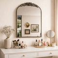 Decorative mirror on a vanity with various items including a vase, makeup, and a small round mirror.