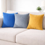 Three colorful pillows (blue, gray, yellow) on a light-colored sofa.
