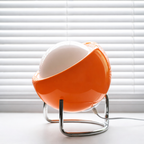 Orange and white spherical lamp on a white surface with white blinds in the background