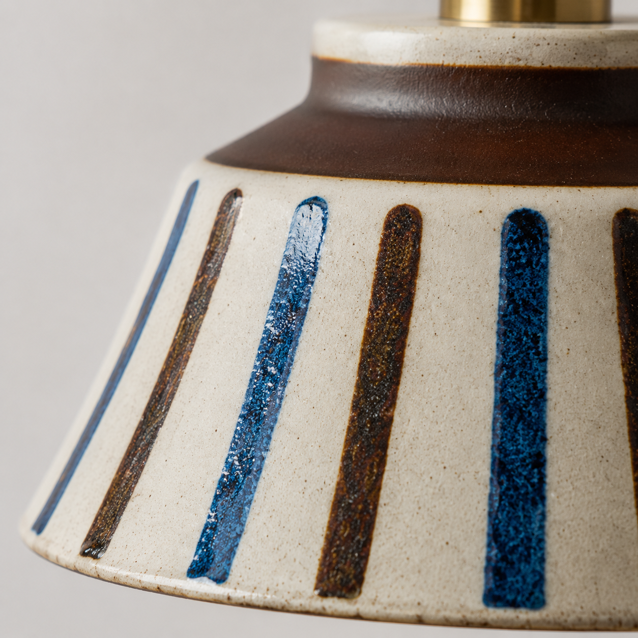 Close-up of a ceramic lampshade with blue and brown stripes on a gray background