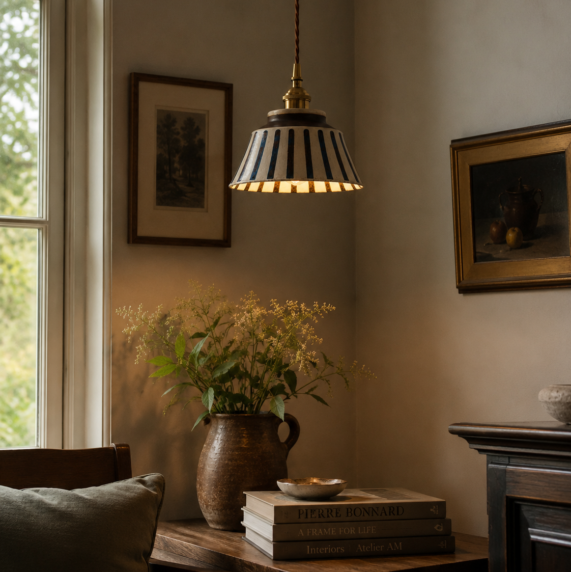 Pendant light hanging above a table with books and a vase in a room with framed pictures on the wall.