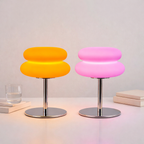 Two colorful stools, one yellow and one pink, on a light surface with a neutral background.