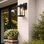 Outdoor wall light fixture on a house exterior with plants and flowers below.