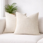 Two beige textured pillows on a white sofa with a plant in the background